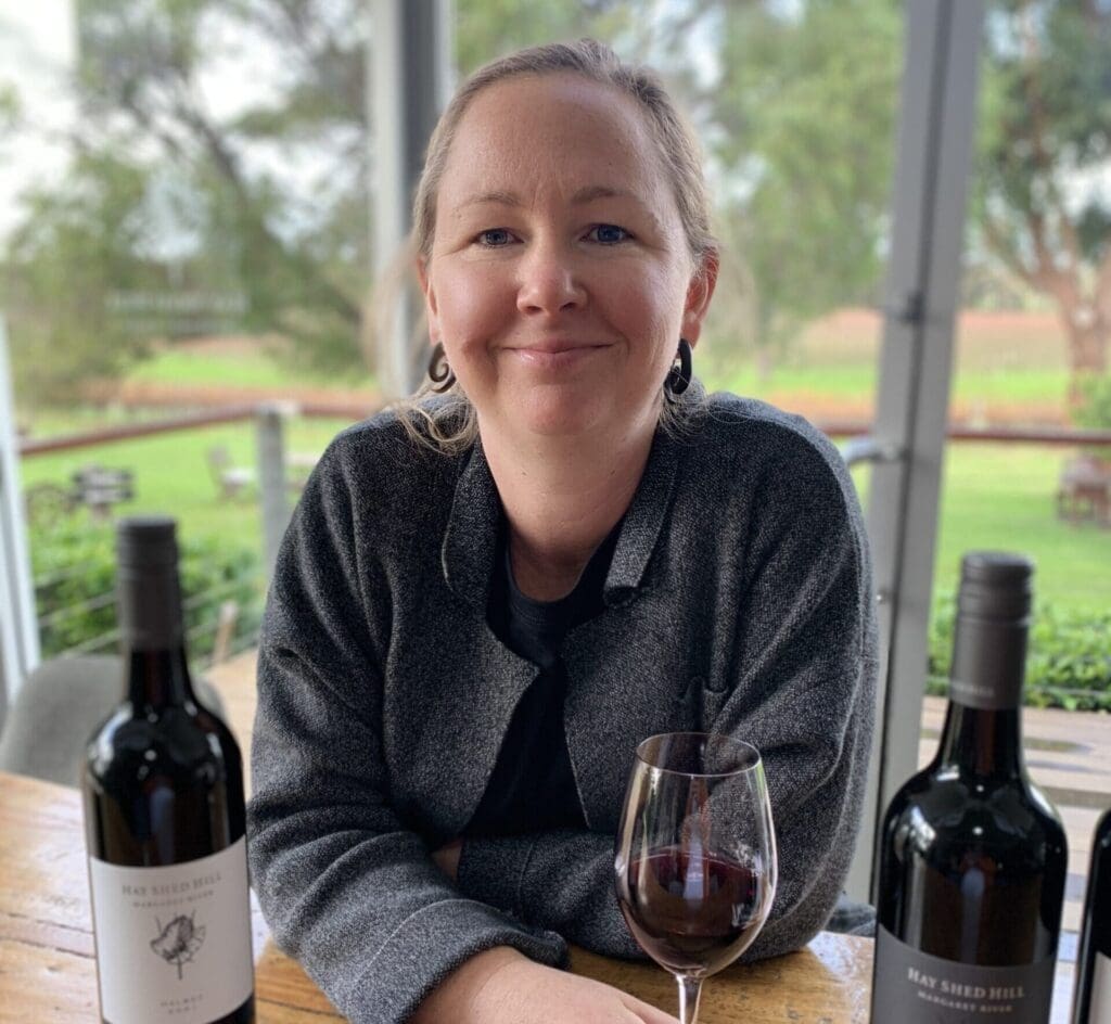 Cara smiling at the camera, she is holding a glass of red wine